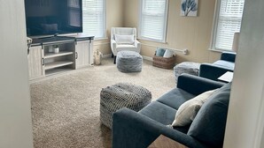 Un soggiorno con televisore a schermo piatto, un divano, pouf, una poltrona e una ventola a soffitto.