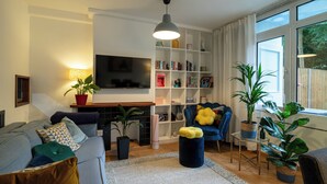 A modern living room with a sofa, armchairs, a TV, a bookshelf, and potted plants.