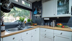 A modern kitchen with white cabinets, a wooden countertop, and a window with a view of palm trees.