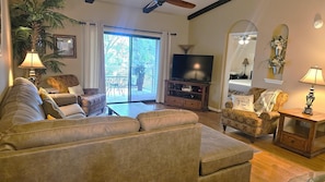 Una sala de estar con sofá, sillón, televisor y vista al exterior.