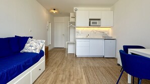 Un espace de vie compact comprenant un coin cuisine, un canapé agrémenté d’un coussin à motifs et un coin repas avec des chaises.
