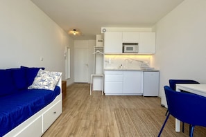 A compact living space with a kitchenette, a sofa with a patterned pillow, and a dining area with chairs.