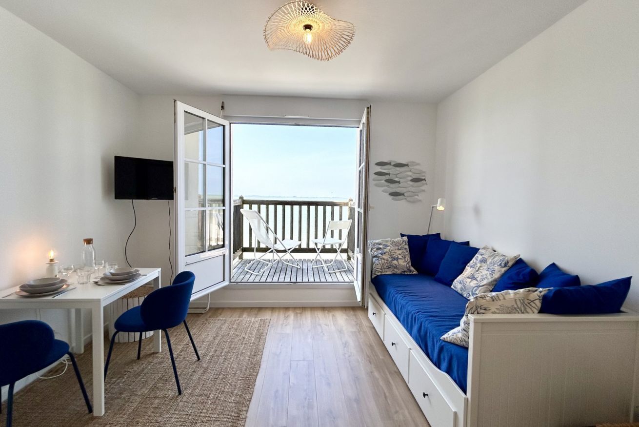 Una habitación con balcón, una mesa de comedor con sillas, un sofá y un televisor.