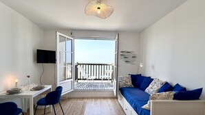 Une chambre avec un balcon, une table à manger avec des chaises, un canapé et un téléviseur.