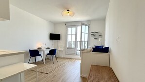 Une pièce moderne et bien éclairée, comprenant un coin repas, un téléviseur et une grande fenêtre.
