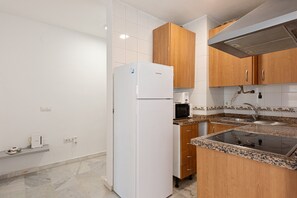 Une cuisine avec des meubles blancs, un réfrigérateur blanc, un four à micro-ondes, un évier et une cuisinière.