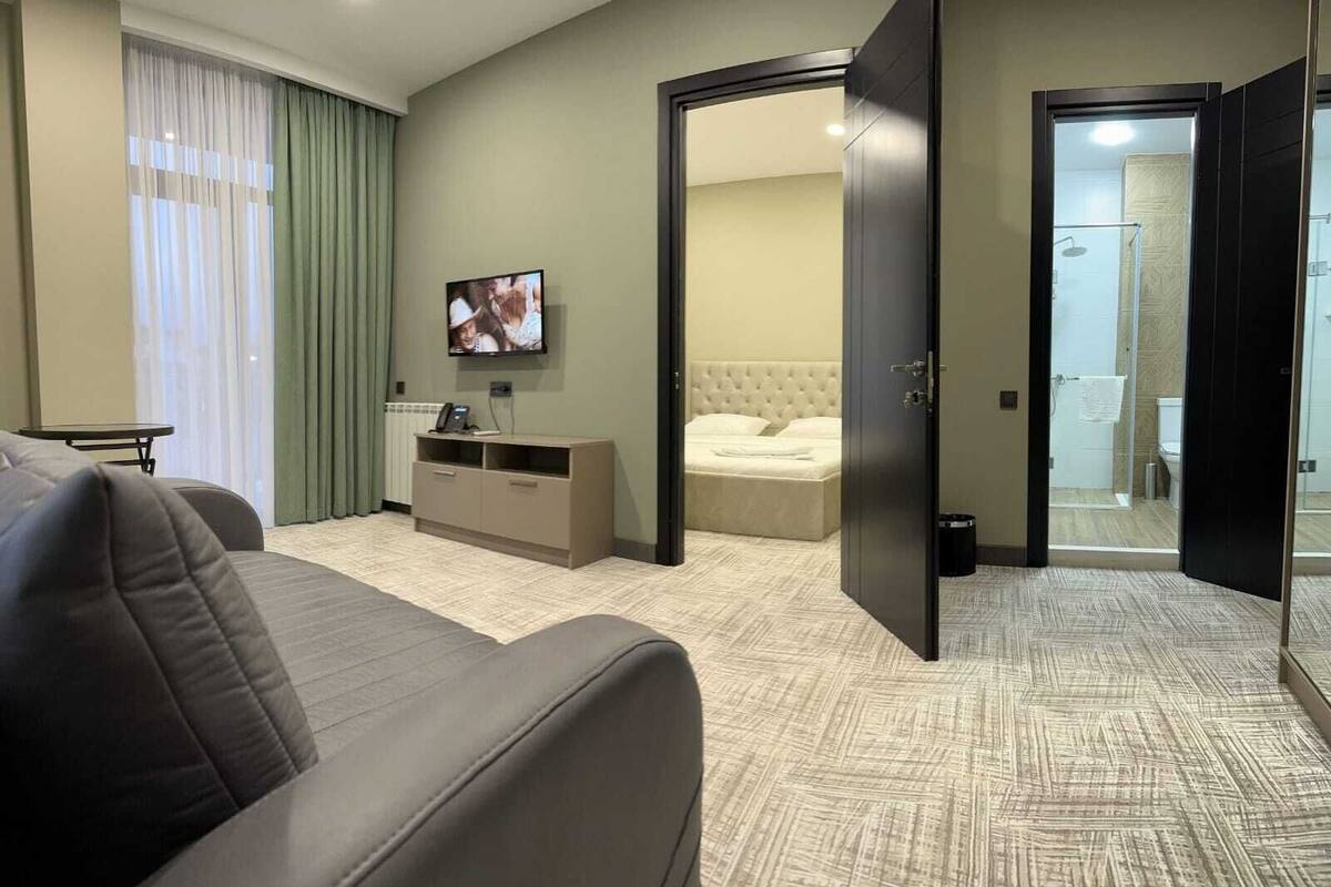 A hotel room with a bed, a TV, a desk, and a bathroom visible through an open door.