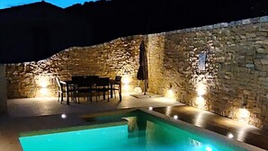 Une piscine avec des murs en pierre et un espace extérieur aménagé pour s’asseoir.