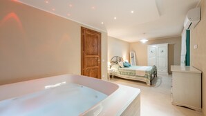 Une chambre avec une grande baignoire, un lit recouvert d’une courtepointe verte et blanche, une armoire et un bureau avec une chaise.
