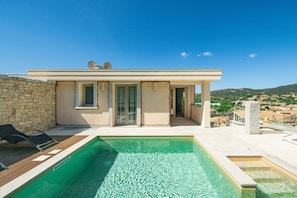 A modern villa with a swimming pool, stone wall, and a view of the countryside.