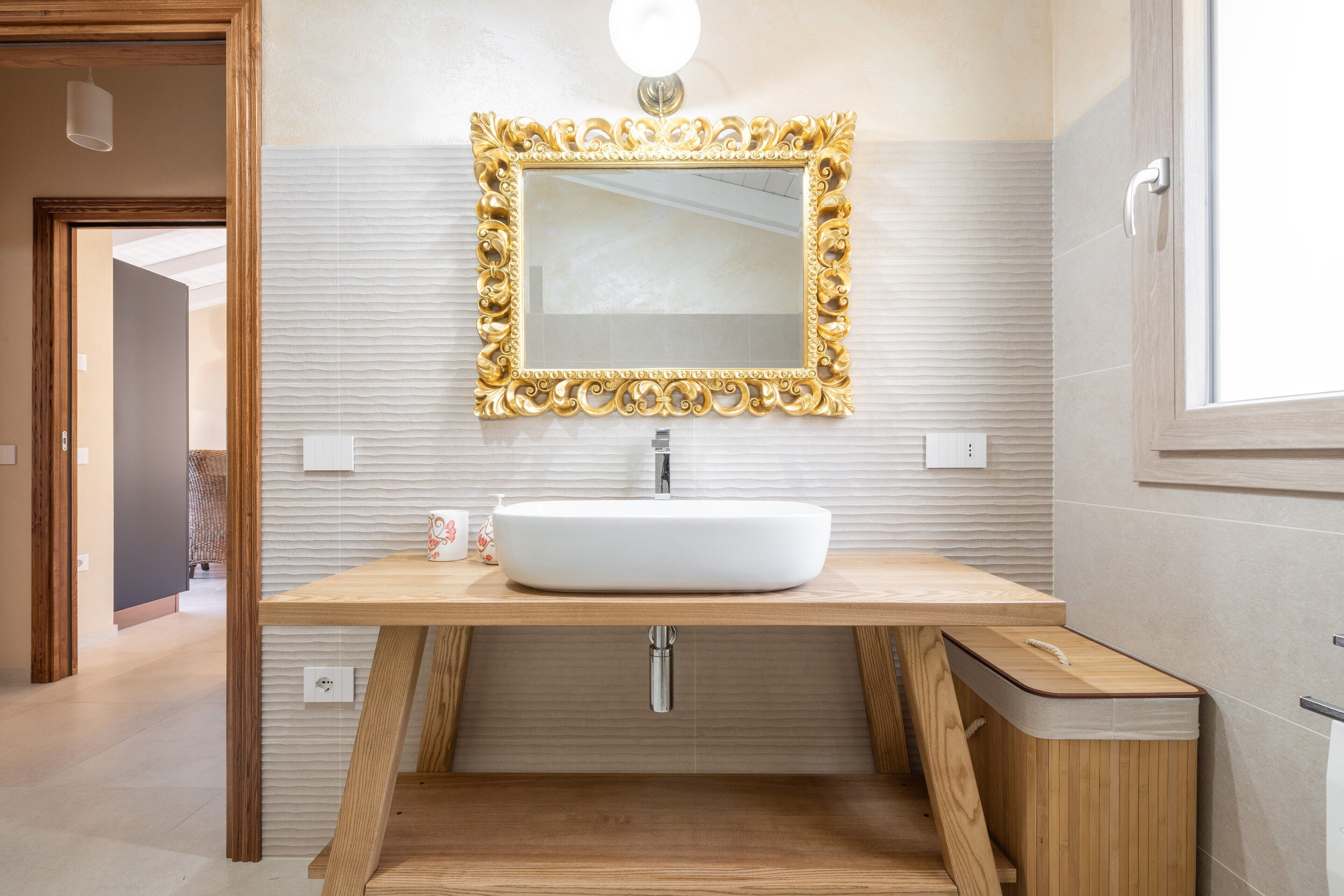 Een moderne badkamer met een houten wastafelmeubel, een witte wasbak en een spiegel met gouden lijst.