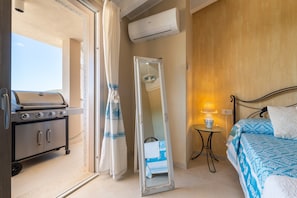 A bedroom with a bed, a nightstand, a mirror, a wall-mounted air conditioner, and a sliding door leading to a balcony.