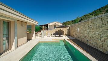 Une piscine avec des chaises longues, un mur en pierre et un bâtiment doté d’un patio couvert.