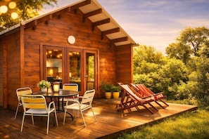 Une cabane en bois avec une terrasse, une table et des chaises, ainsi que deux fauteuils de jardin.