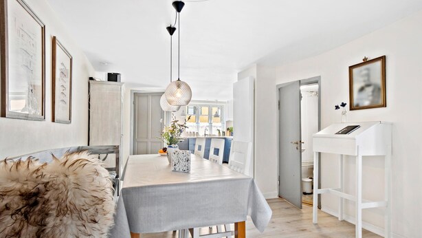 A modern kitchen with white cabinetry, a dining table with a striped tablecloth, and a hanging light fixture. - 3 bedroom lovely home in Faaborg (Faaborg)
