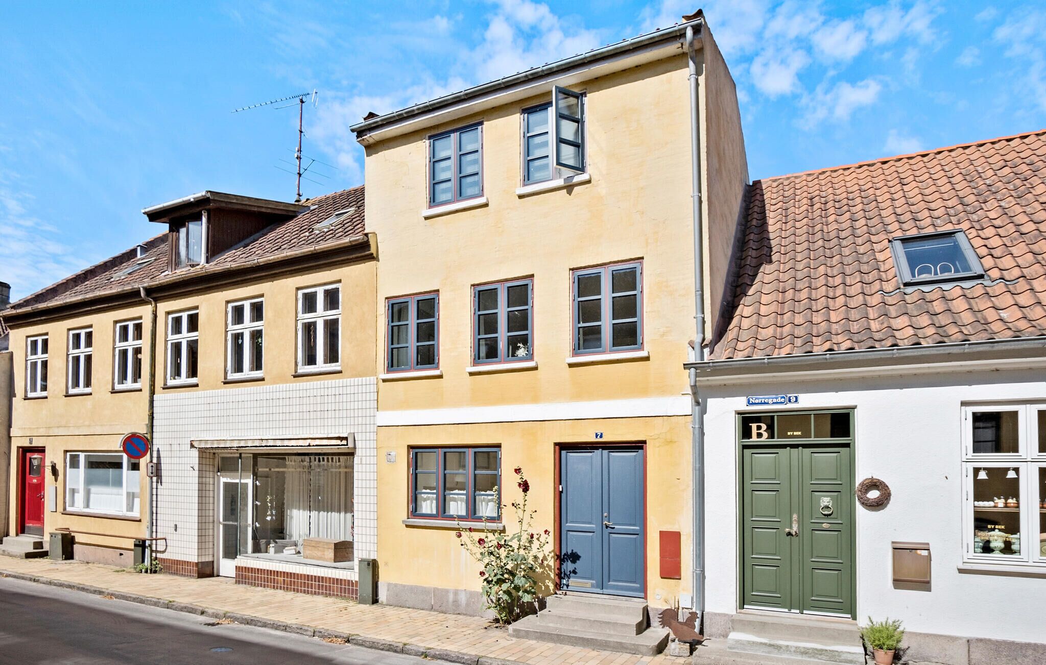 En rad byggnader i europeisk stil med tydliga arkitektoniska särdrag, inklusive en gul byggnad med en blå dörr och en grön dörr, samt en vit byggnad med en skylt som visar "Nerregade 9".