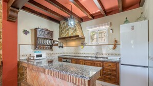 Una cocina con encimera de granito, una isla de ladrillo, armarios de madera, horno empotrado y refrigerador.