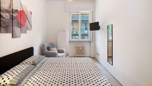 Ein Schlafzimmer mit einem Bett, einem Sessel, einem Heizkörper, einem Fenster und einem an der Wand montierten Fernseher.