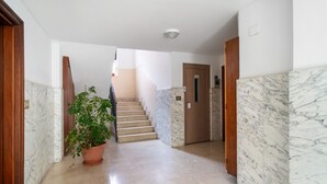 Ein Flur mit Marmorwänden, einer Zimmerpflanze, einer Holztür und einer Treppe.
