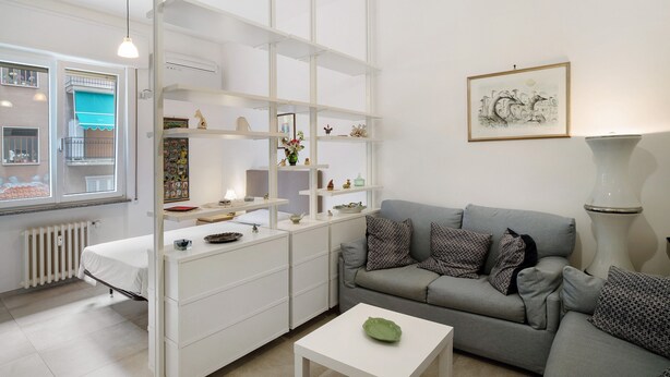 Ein modernes Wohnzimmer mit einem grauen Sofa, weißen Möbeln und einem gerahmten Kunstwerk an der Wand.