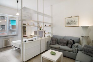 Un salon moderne avec un canapé gris, des meubles blancs et une œuvre d’art encadrée accrochée au mur.
