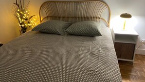 A bed with a patterned bedspread, two pillows, a bedside lamp, and a small nightstand with a lamp. - COSY Belleville briapartment (Paris)