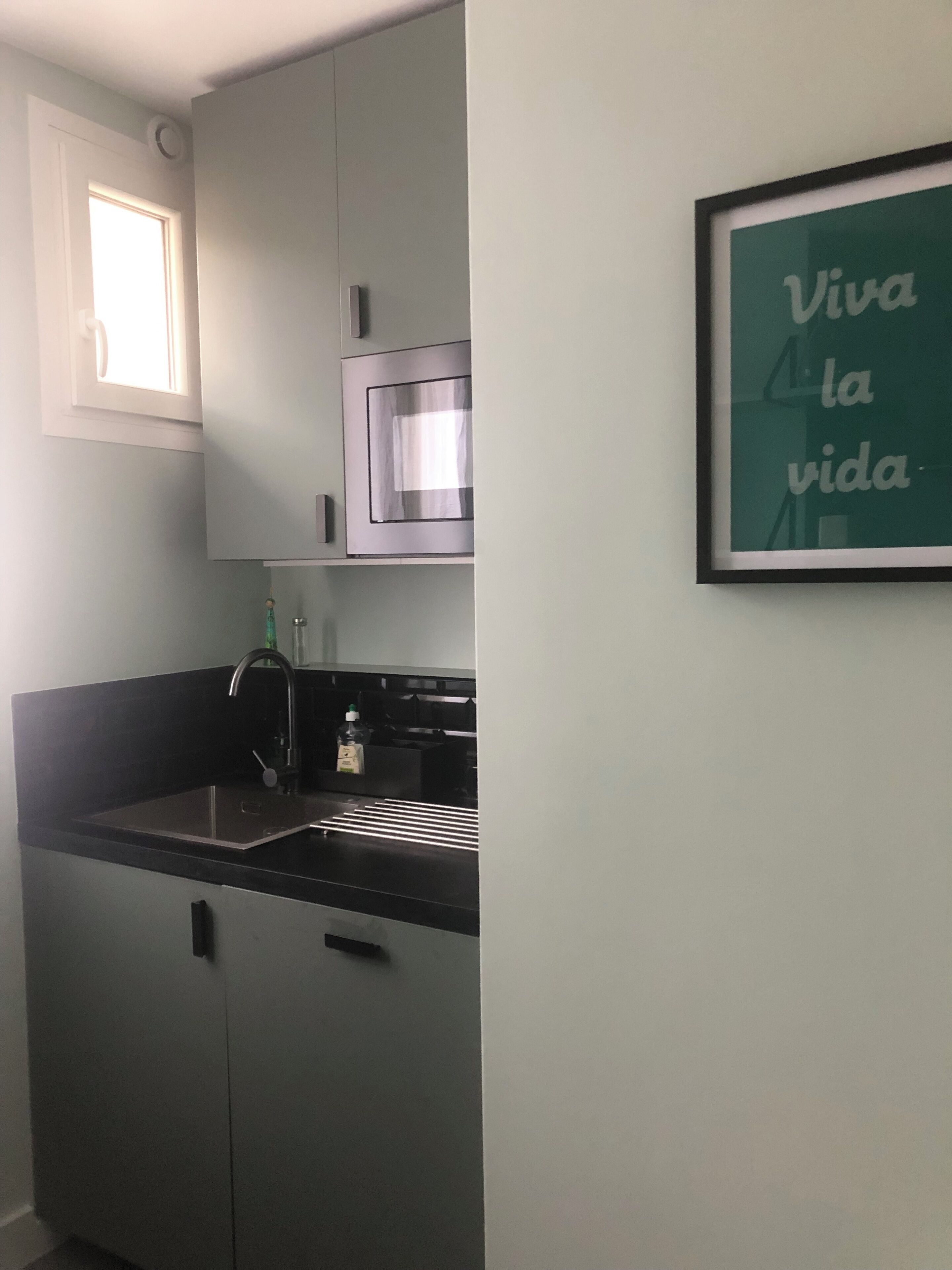 A small kitchen with a sink, a microwave, and a framed sign on the wall.