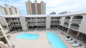 Un patio de hotel con piscina, tumbonas y vistas a edificios altos circundantes.