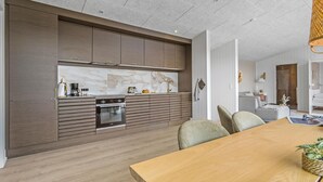 Een moderne keuken met een inbouwoven en een eethoek met een houten tafel.