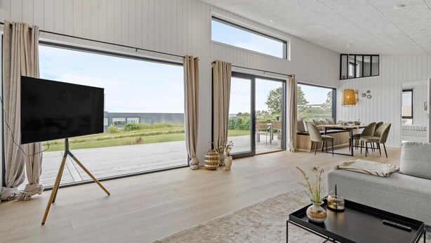 Een ruime woonkamer met een grote televisie op een statief, een bank, een salontafel en een eethoek met tafel en stoelen.