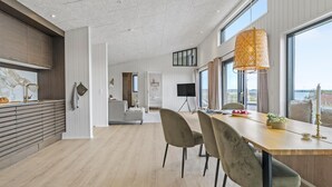 Een ruime keuken met een groot eiland, een eethoek met een houten tafel en stoelen, en uitzicht op de zee door grote ramen.