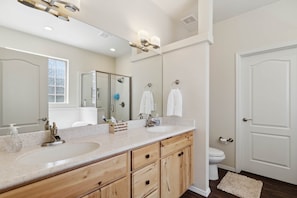 A bathroom with a double sink vanity, a large mirror, a toilet, and a door. - Woodland Haven | On Golf Resort | 10 min Bearizona (Williams)