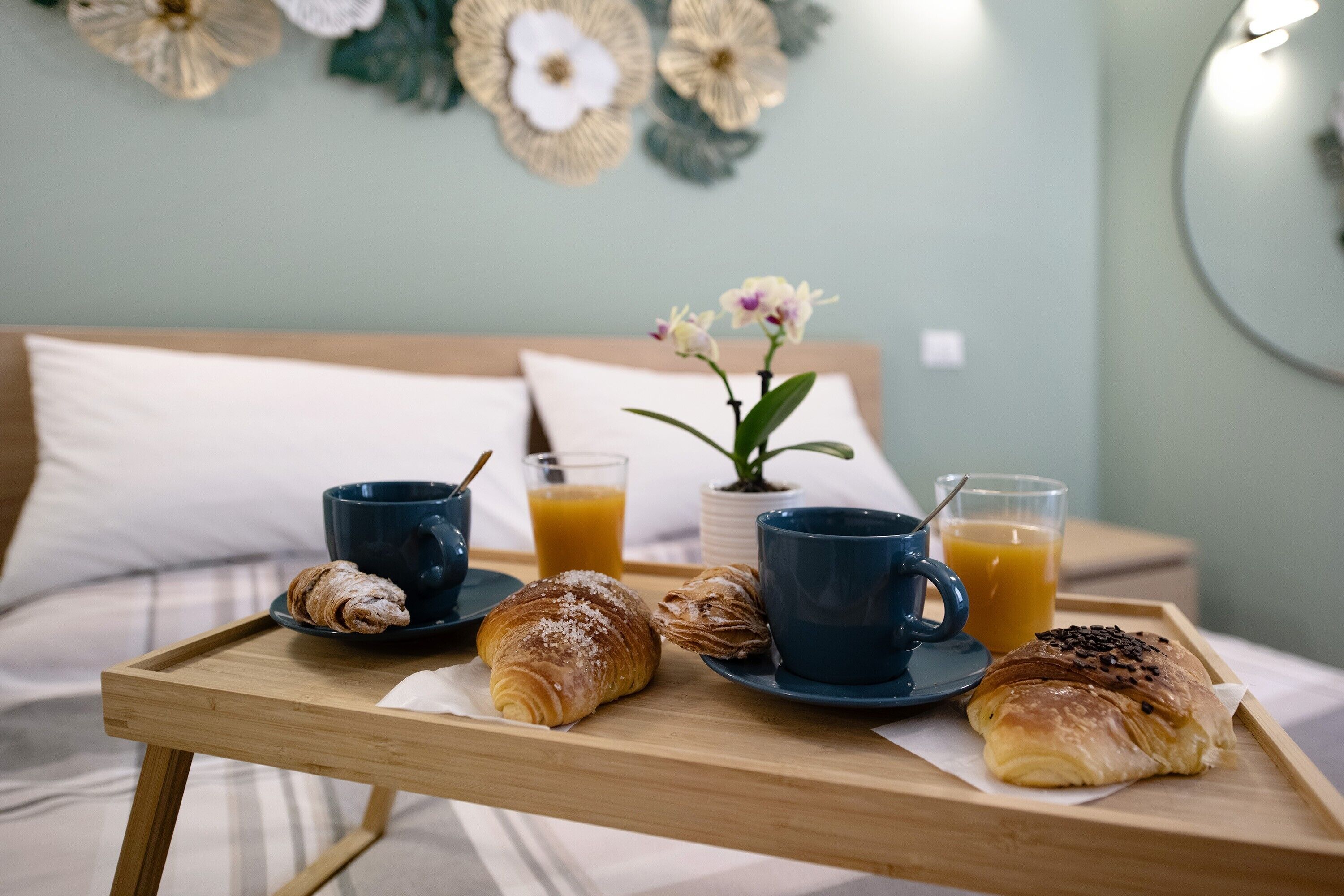 Ein Frühstücksbrett mit Croissants und Saft auf einem Bett mit Kissen und einer Wanddekoration.