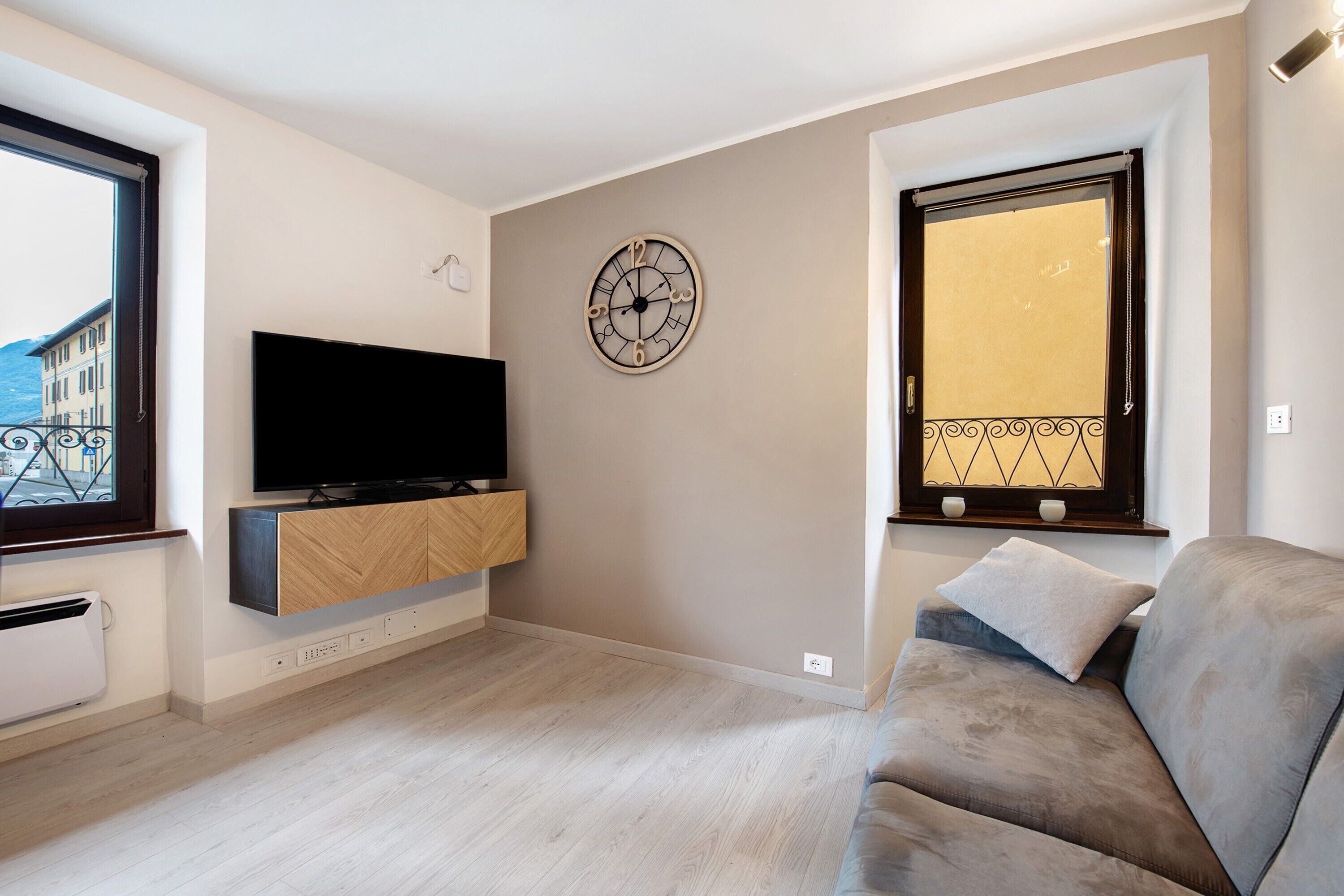 Uma sala de estar moderna com televisão de tela plana, relógio de parede e uma grande janela com grade decorativa.