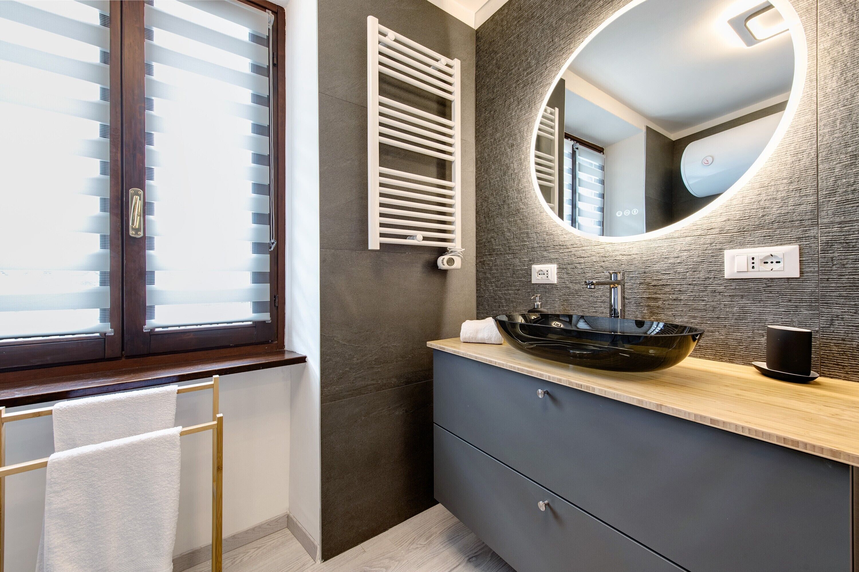 Un baño moderno con un espejo grande, un lavamanos tipo cuenco negro y un perchero para toallas.