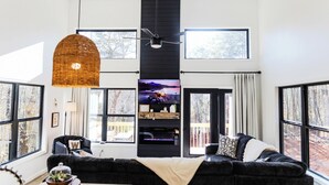Een moderne woonkamer met een zwarte modulaire bank, een open haard, een grote televisie en grote ramen met uitzicht op de omgeving.