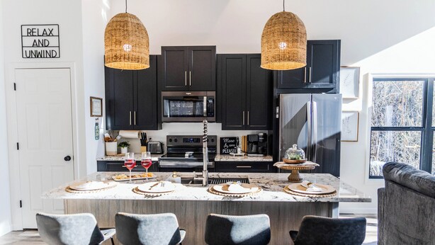 Een moderne keuken met donkere kastjes, een centraal eiland met barstoelen, een magnetron en een koelkast.