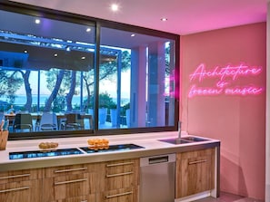 A modern kitchen with a large window, wooden cabinets, and a neon sign stating 'Architecture is green music.'