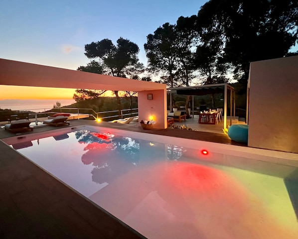 An infinity pool with a sunset view, outdoor seating, and a pergola.