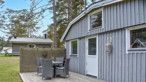 A wooden deck with wicker furniture, a metal railing, and a grey building with windows and a door. - Beautiful home in åhus with WiFi (Åhus)