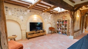 A cozy living room with a stone wall, wooden beams, a television, a bookshelf, and a fireplace.