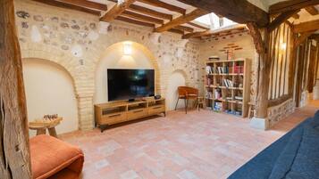 A cozy living room with a stone wall, wooden beams, a television, a bookshelf, and a fireplace.