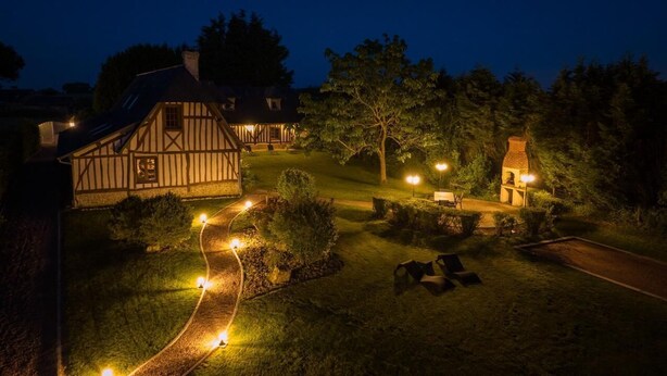 A traditional half-timbered house with a well-lit pathway leading to a seating area.