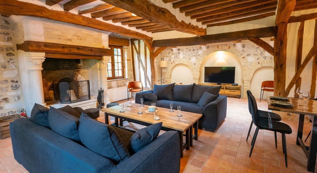 A rustic living room with stone walls, wooden beams, a fireplace, a television, and a dining area with a table and chairs.