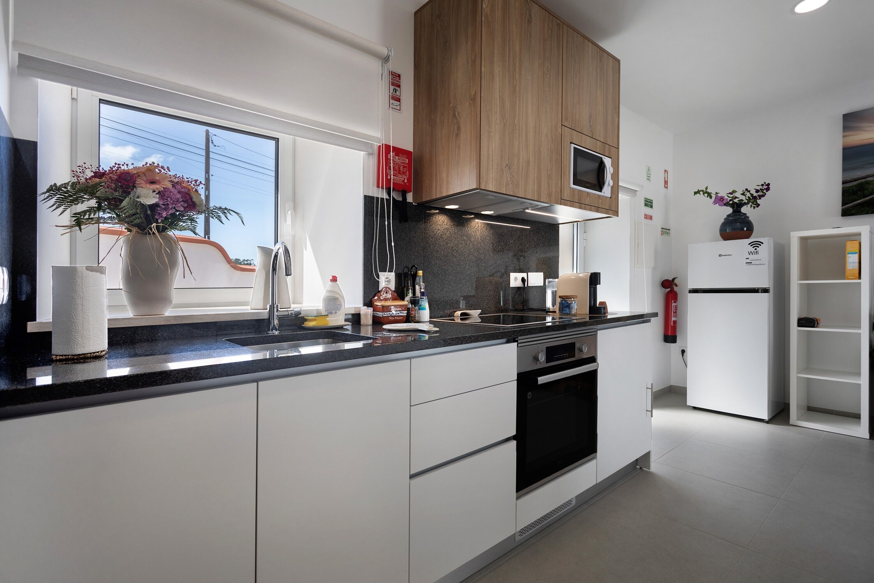A modern kitchen with white cabinets, a black countertop, a microwave, and a built-in oven.