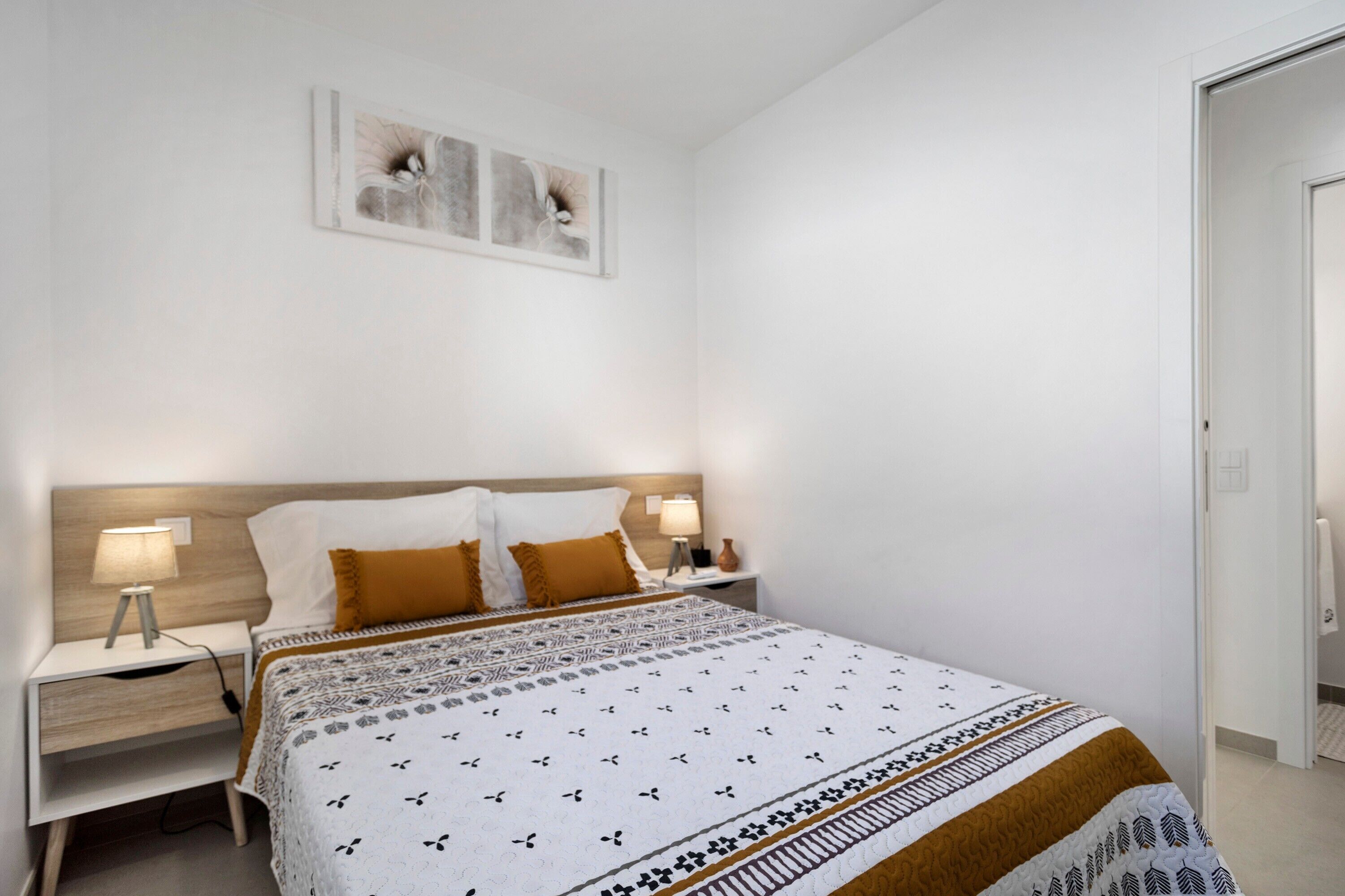 Une chambre à coucher comprenant un lit, des tables de chevet, une œuvre d’art accrochée au mur et une porte.