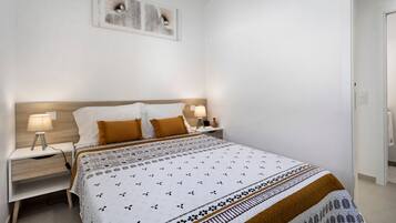 Une chambre à coucher comprenant un lit, des tables de chevet, une œuvre d’art accrochée au mur et une porte.