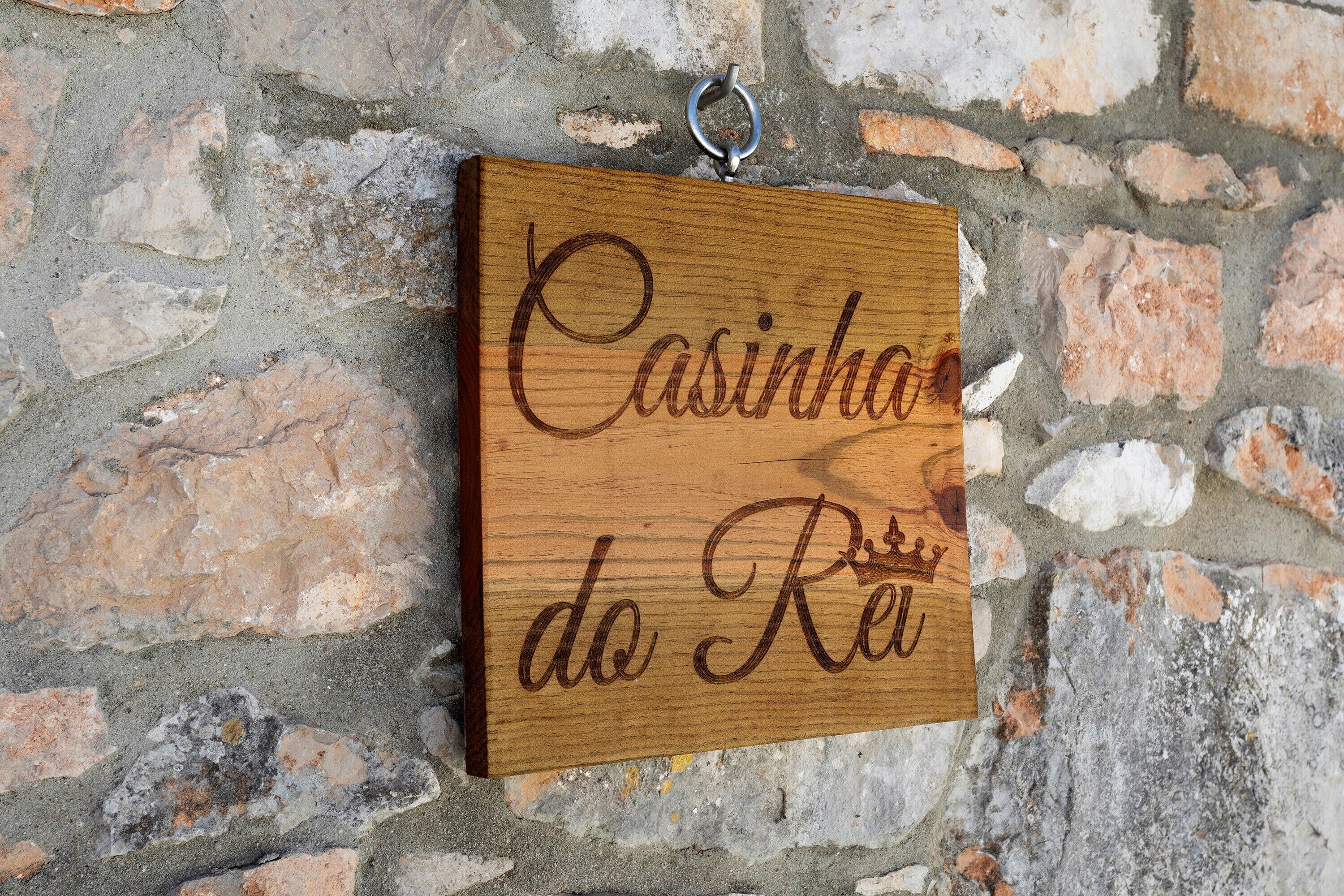 Een houten plaquette met de tekst 'Casinha do Rei' bevestigd aan een stenen muur.