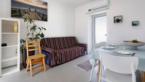 A modern living room with a sofa, a dining table set for two, a bookshelf, and a potted plant. - Apartment 'Casinha Do Rei' with Shared Terrace, Wi-Fi and Air Conditioning (Fátima)