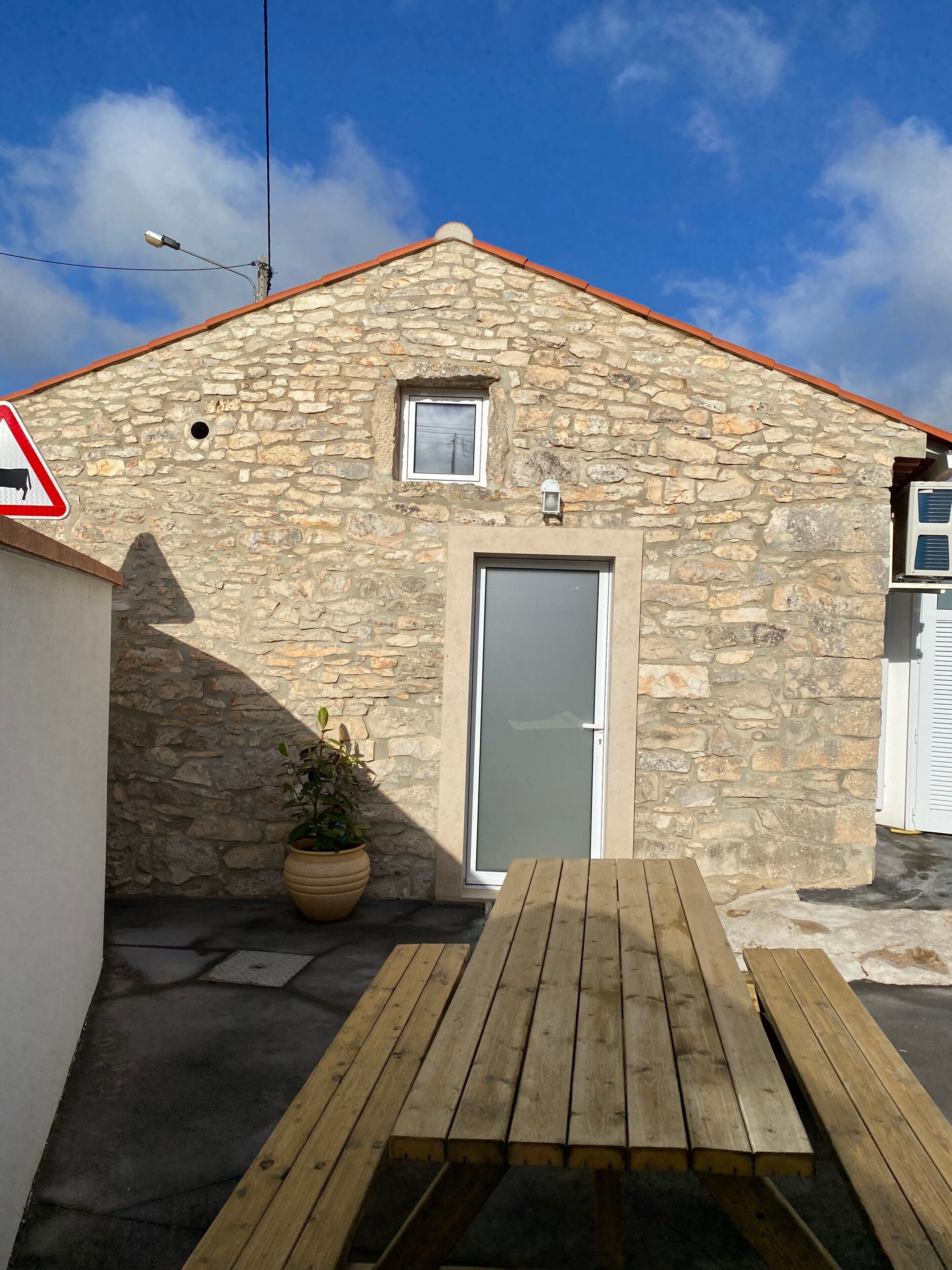 A stone building with a red roof, a door, a small window, a street sign, and a wooden bench.